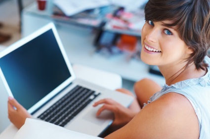 Woman wearing a short sleeve blue denim top working on her laptop computer and looking up over her shoulder.