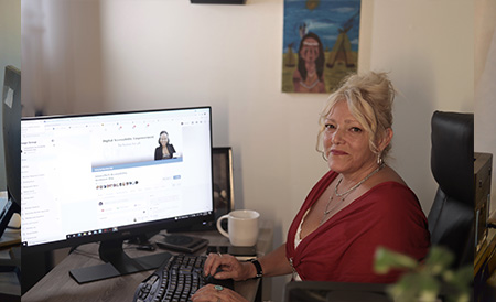 Photo of Nathalie Mallette sitting at a desk and working on a computer with the LinoraTech Inclusion website showing on her computer monitor.