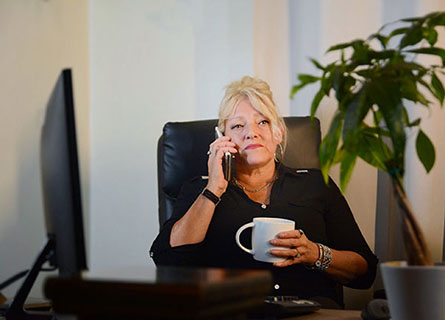 Photo of Nathalie Mallette sitting at a desk and holding a coffee cup in her hand.
