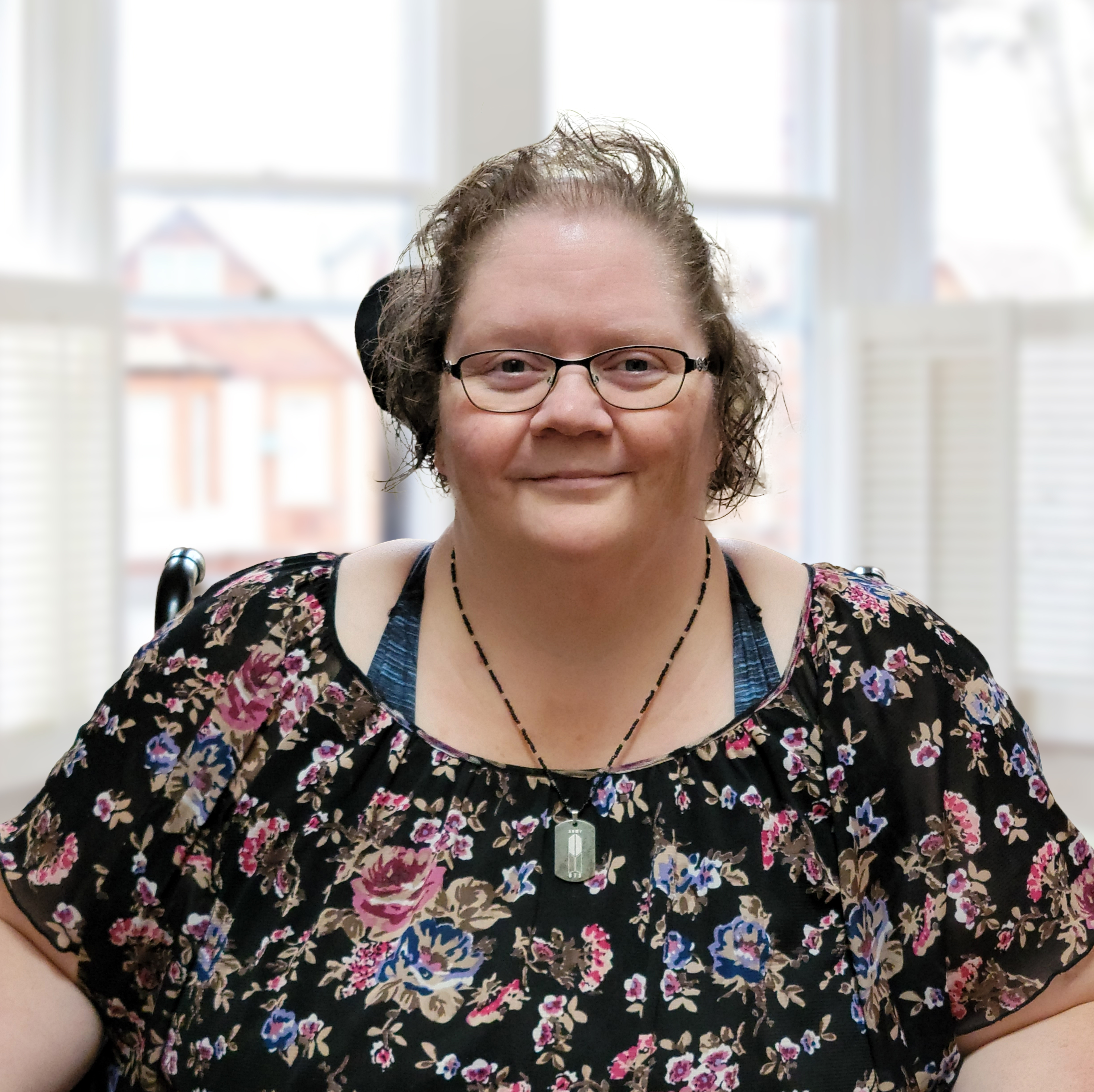 Photo of Rosella Derksen seated indoors with a wall of windows in the background creating a well-lit and comfortable setting. 