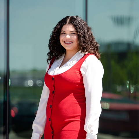 Photo of Kerry wearing a red dress and standing in front of a commercial building.