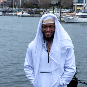Photo of Hakeem smiling, standing outside with a marina behind him.