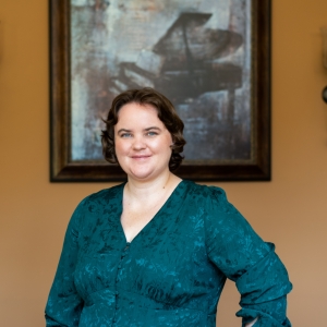 Photo of Katherine wearing a green dress standing indoors with an abstract painting in the background.